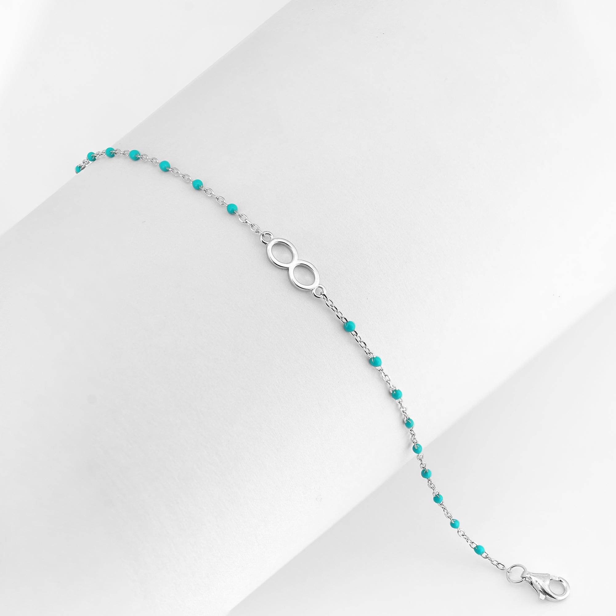 A delicate silver bracelet with turquoise beads and an infinity symbol shown on a white background.