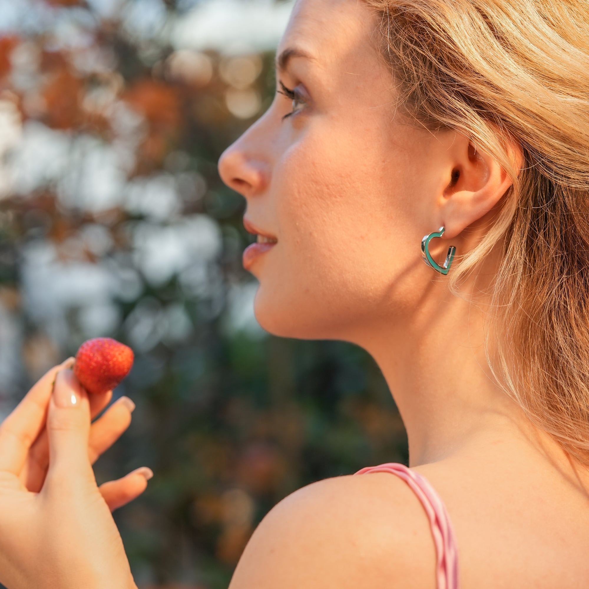 Woman wearing Electric Enamel Heart Hoop Earrings with a minimalist outfit, showcasing the bold teal enamel heart shape.