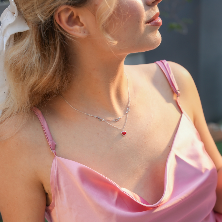 Woman wearing the Hearts in Harmony double-layered silver necklace with red enamel heart pendant, styled with a sweetheart neckline.