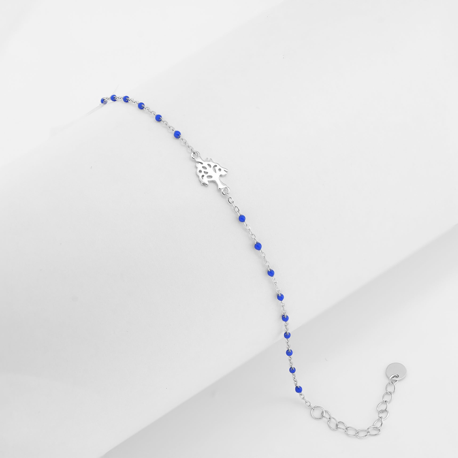 A delicate bracelet featuring a silver floral centerpiece and royal blue beads on a white background.