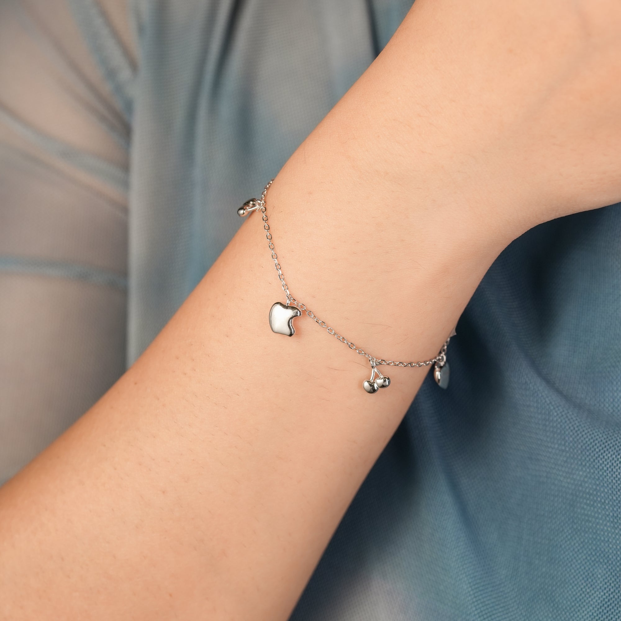 Woman styling the Apple-Cherry Fruit Charm Bracelet on wrist, paired with a casual outfit, showcasing the playful, summer-inspired silver design.