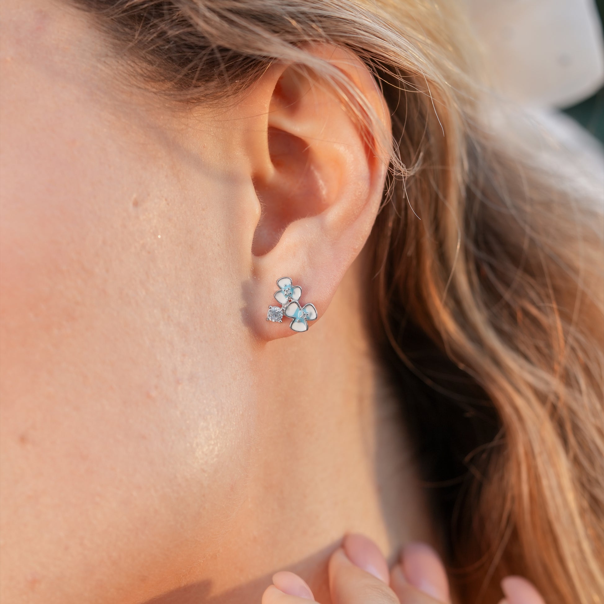 Floral enamel stud earrings styled on a woman with a soft updo and pastel outfit.