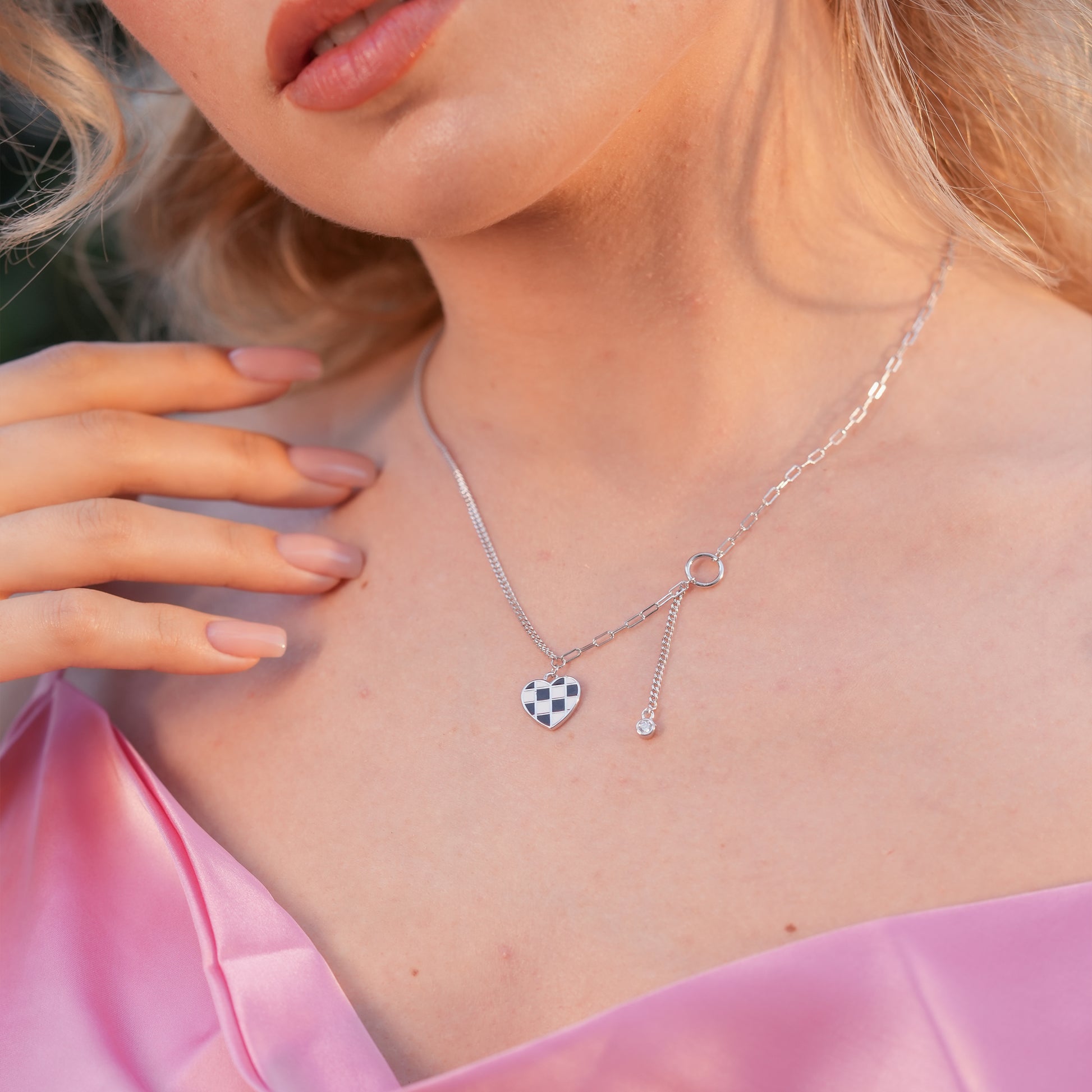 Model wearing the Checkmate Heart Y-Link Necklace with a black & white enamel heart pendant and crystal drop, styled for a trendy streetwear look.