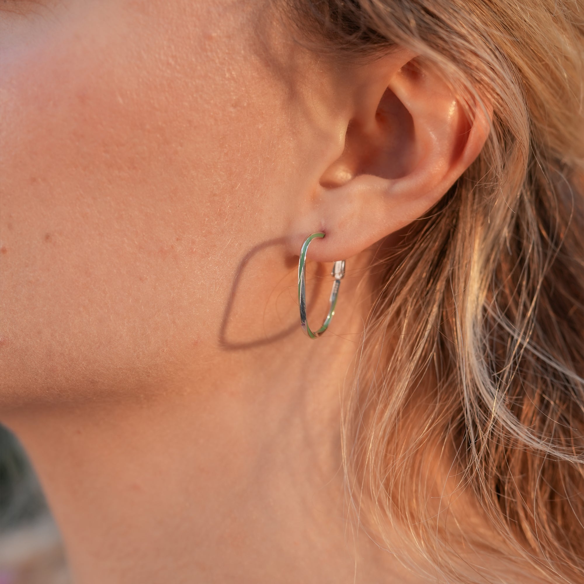Model wearing Lagoon Hoop Earrings styled with a white shirt, highlighting the green enamel accents.