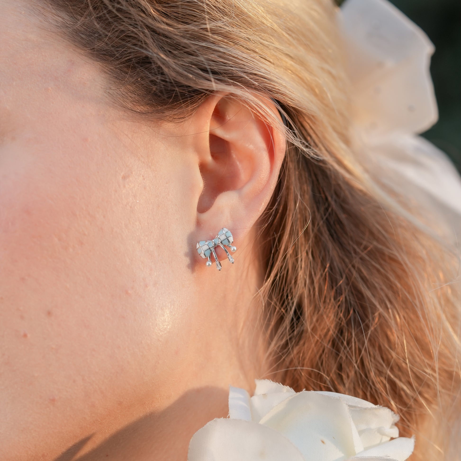 Retro-inspired bow drop earrings with dangling pearls styled on a woman in a pastel outfit.