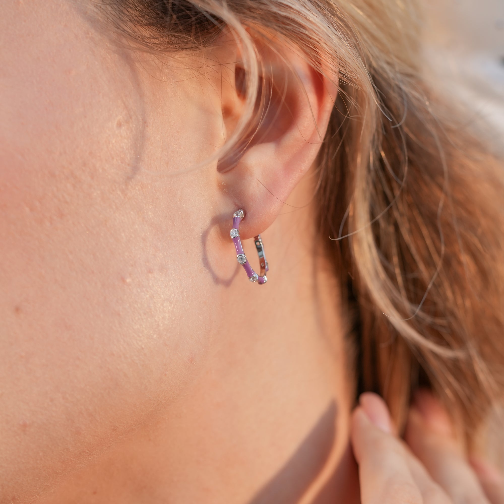Close-up of woman wearing purple enamel half-hoop earrings, styled with a casual chic outfit.