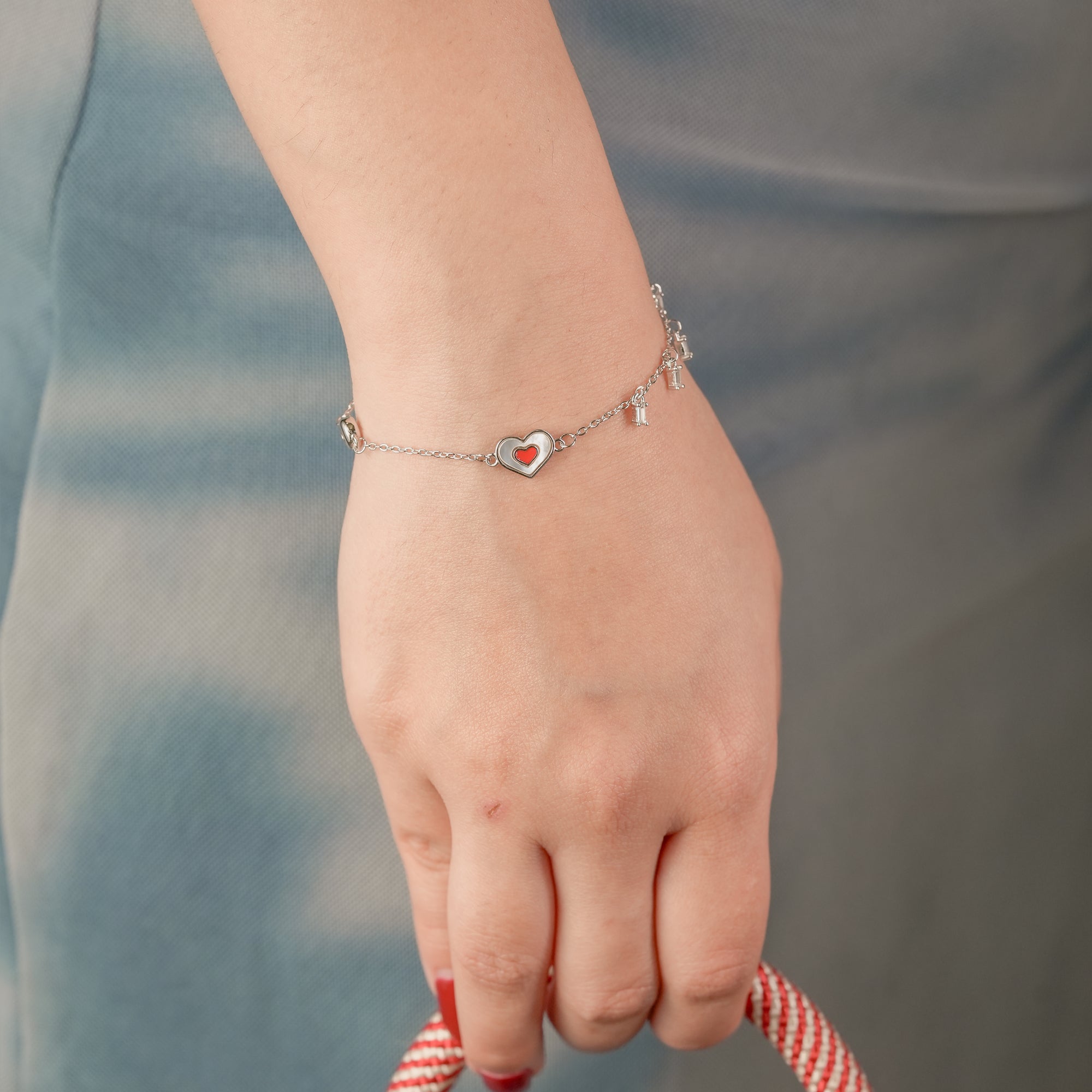 Elegant sterling silver bracelet with red heart charm worn on wrist – dainty and stackable style by IHA Fine Jewellery