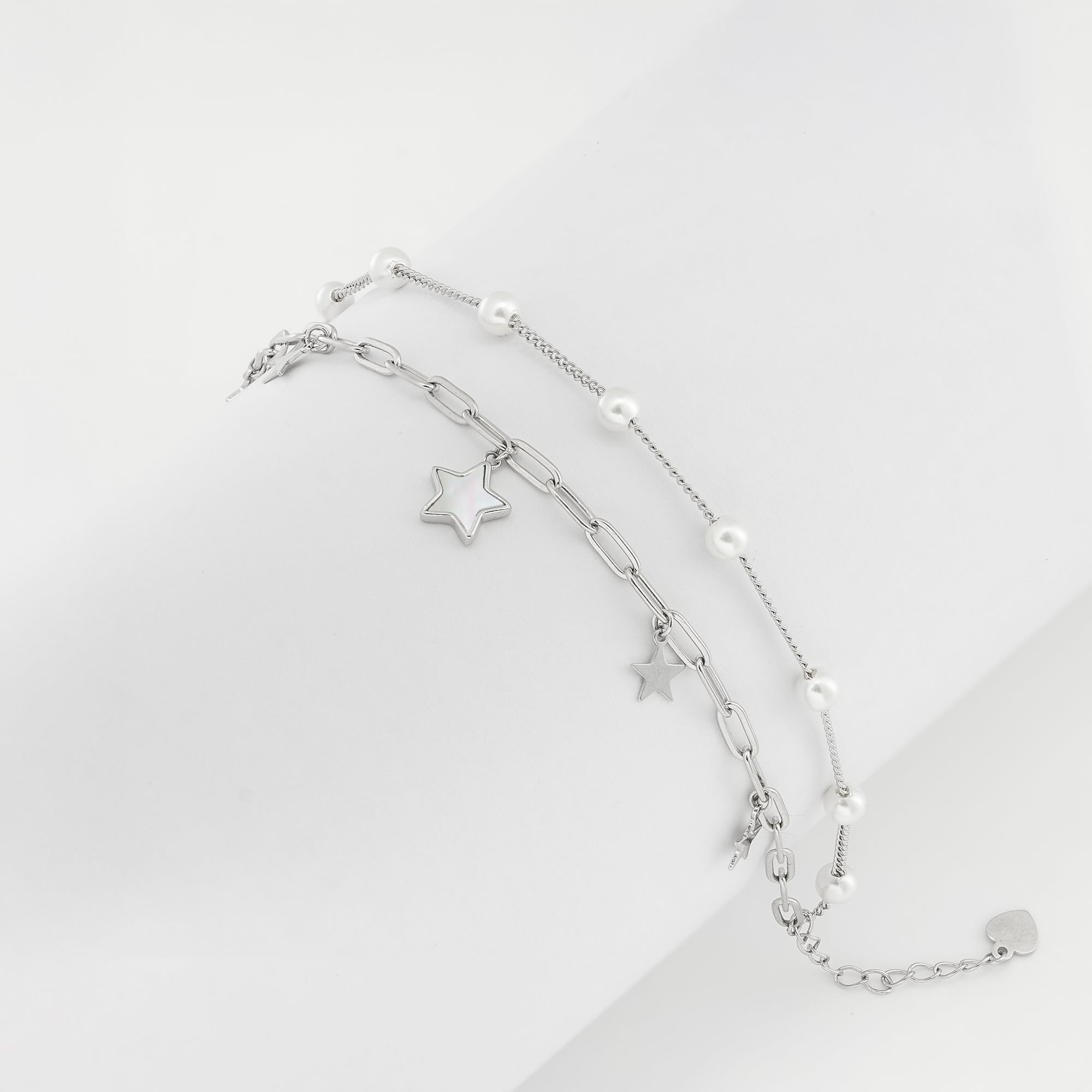  Dual-strand silver bracelet featuring pearls and star charms, displayed on a soft neutral backdrop.

