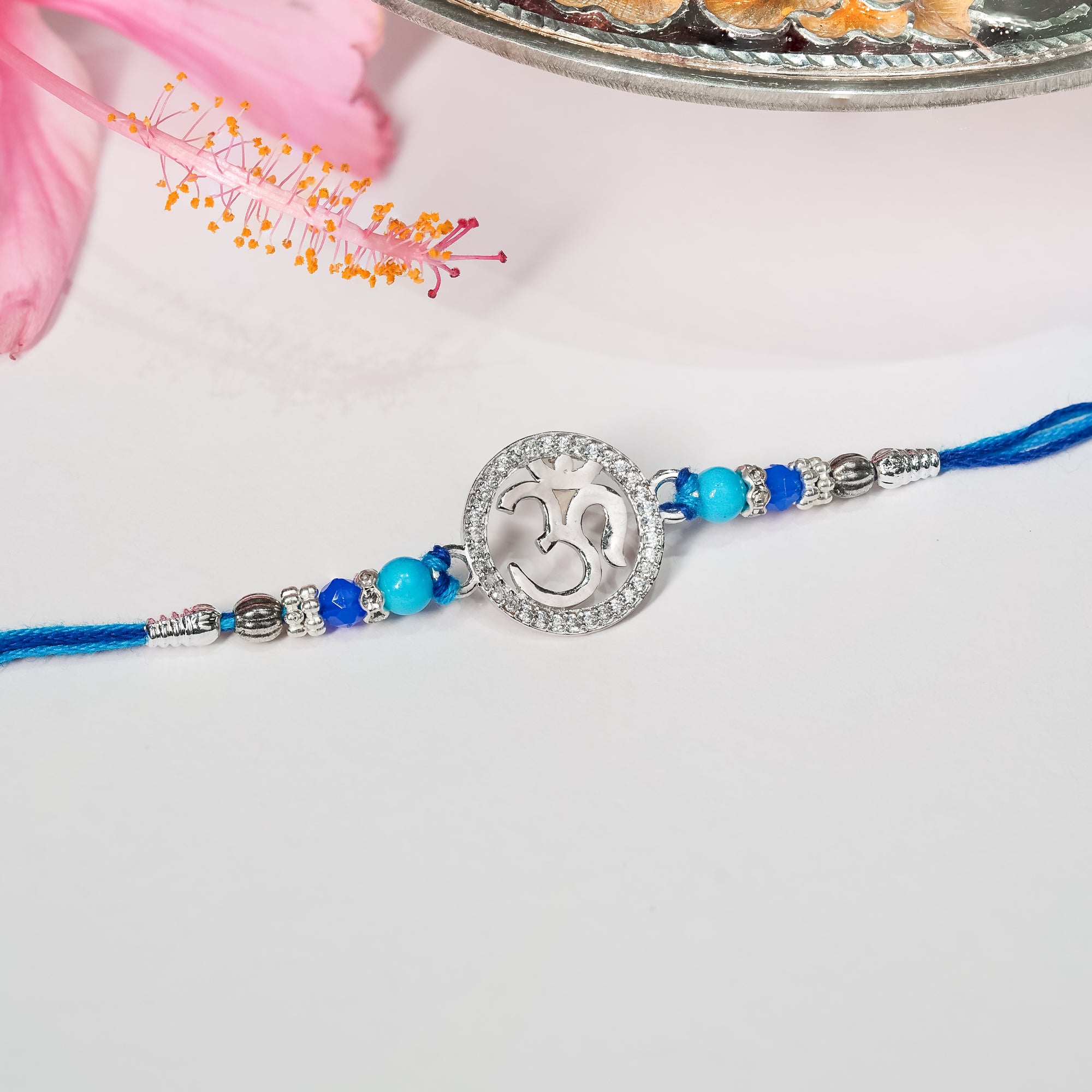 925 silver rakhi with Om symbol placed on traditional thread in earthy tones.