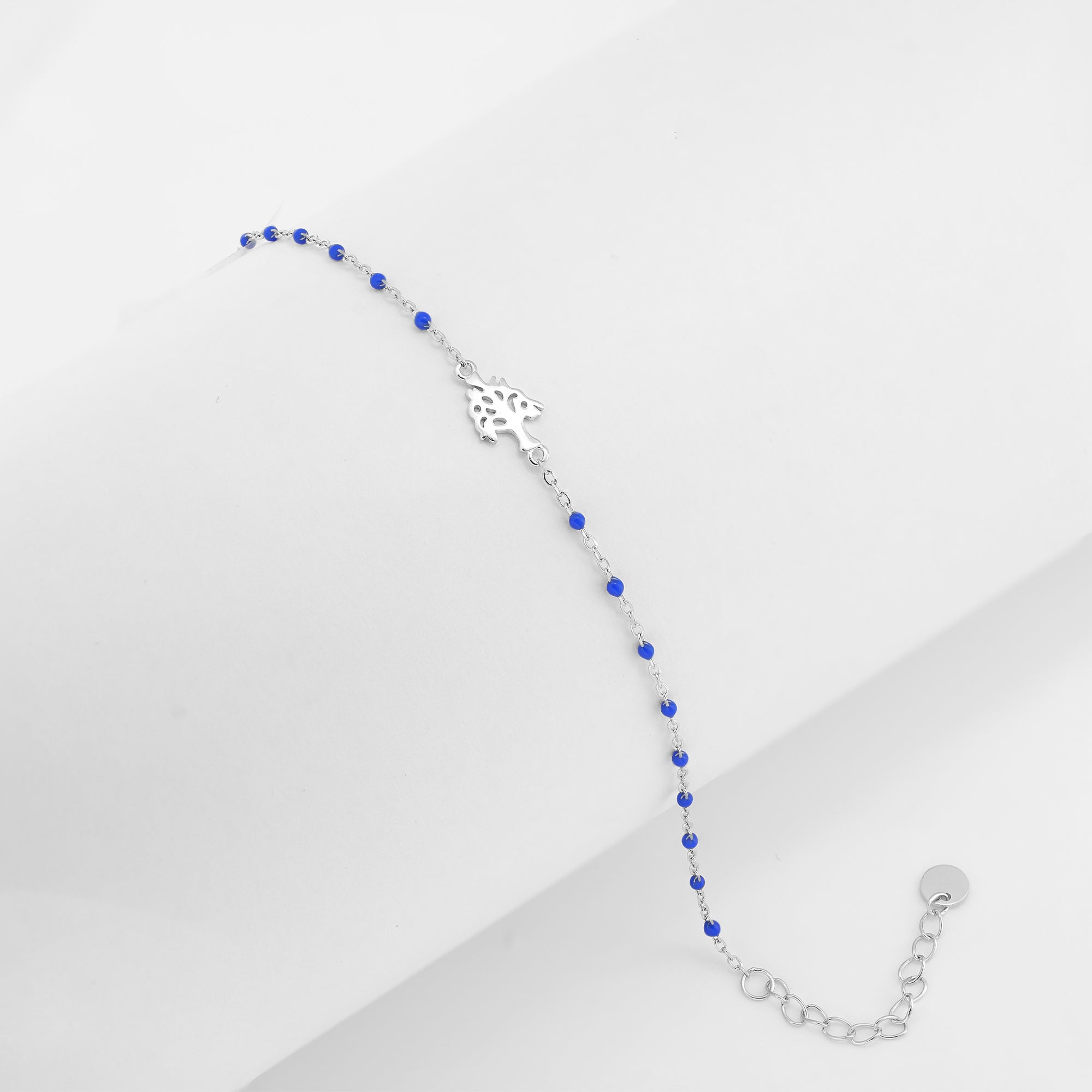 A delicate bracelet featuring a silver floral centerpiece and royal blue beads on a white background.