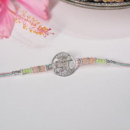 Silver rakhi with Shree symbol on saffron-red thread, displayed on minimal background.

