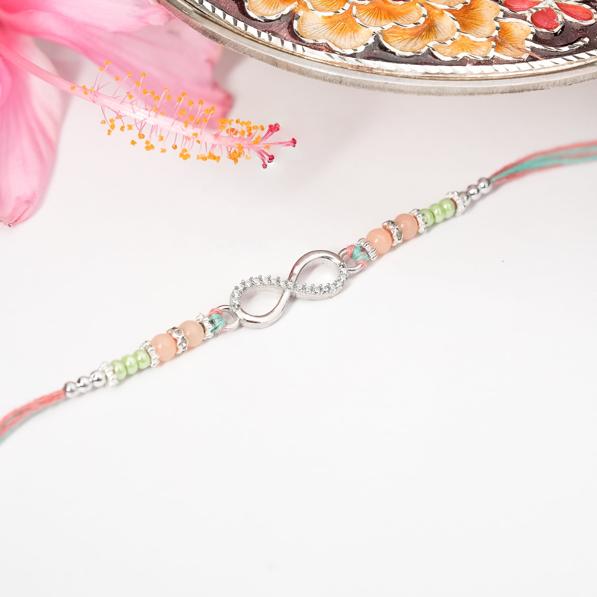 Close-up of Silver Infinity Rakhi featuring a sterling silver infinity charm on pastel pink and lilac threads, placed on white background.