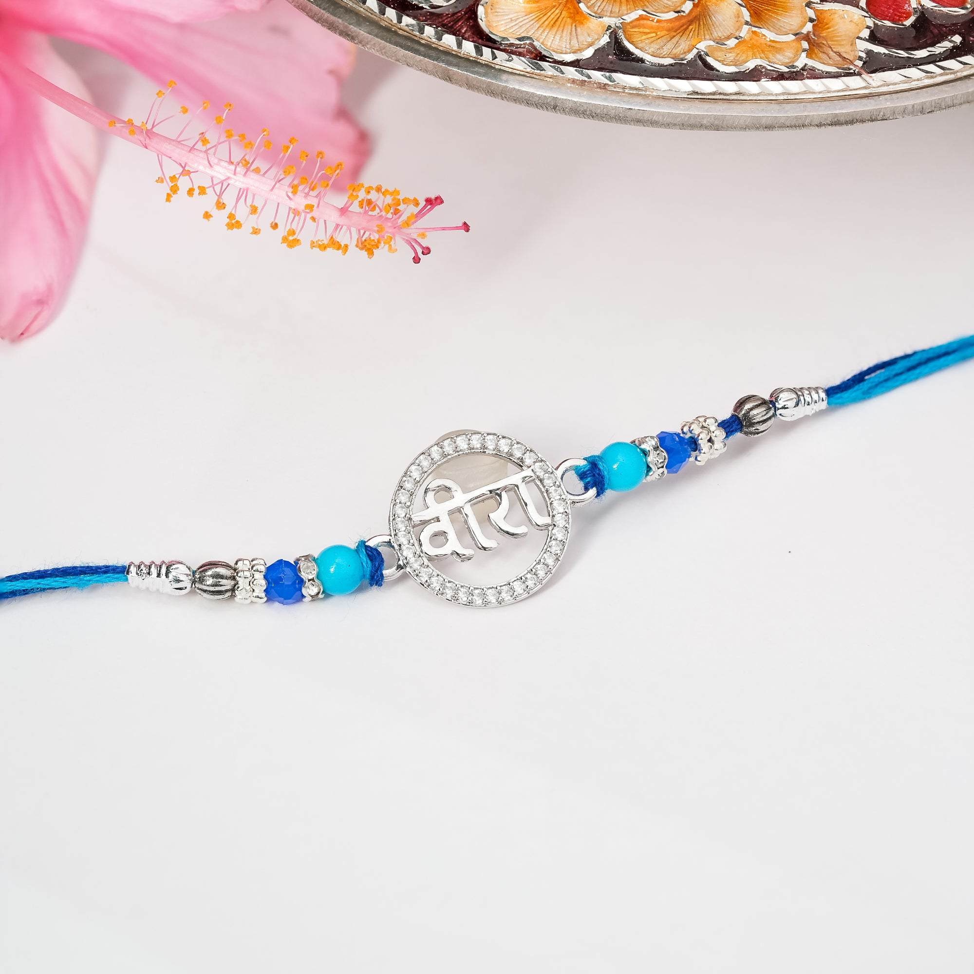 Rakhi in sterling silver with symbolic centerpiece tied on soft thread, displayed on plain background.

