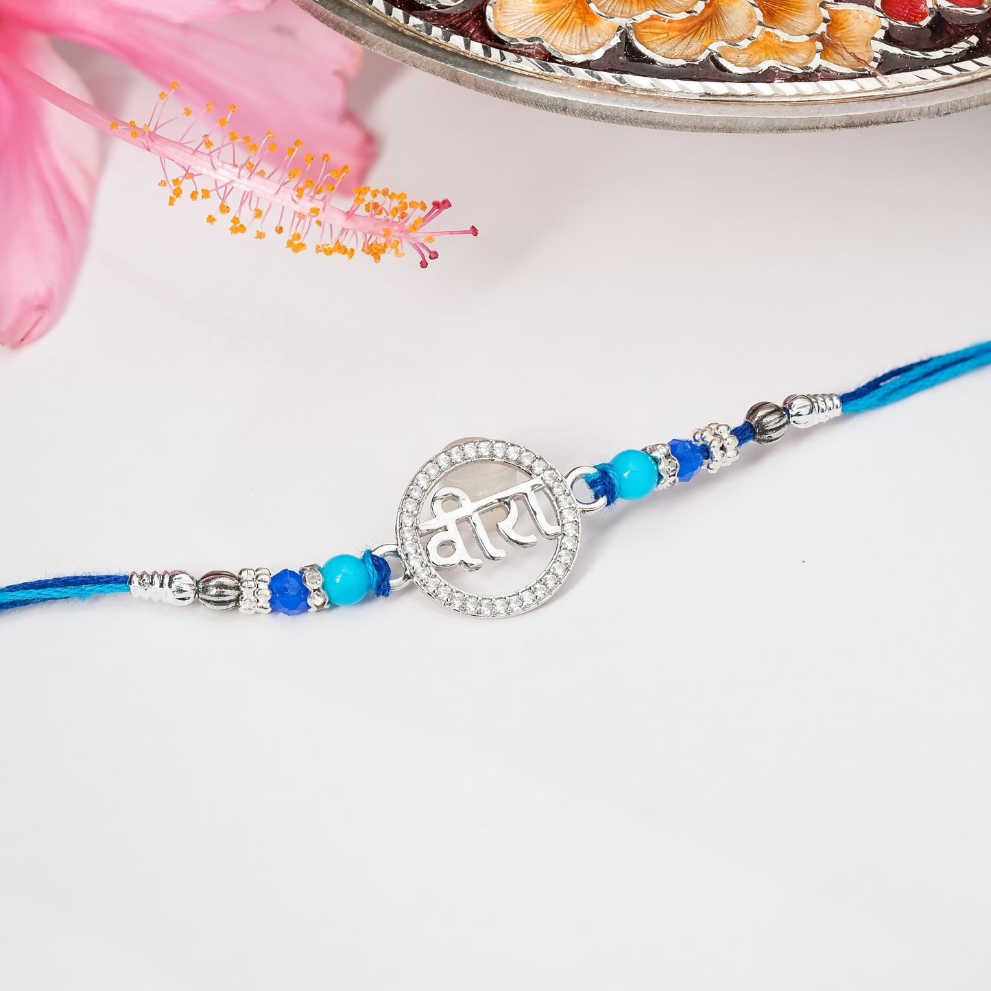 Rakhi in sterling silver with symbolic centerpiece tied on soft thread, displayed on plain background.

