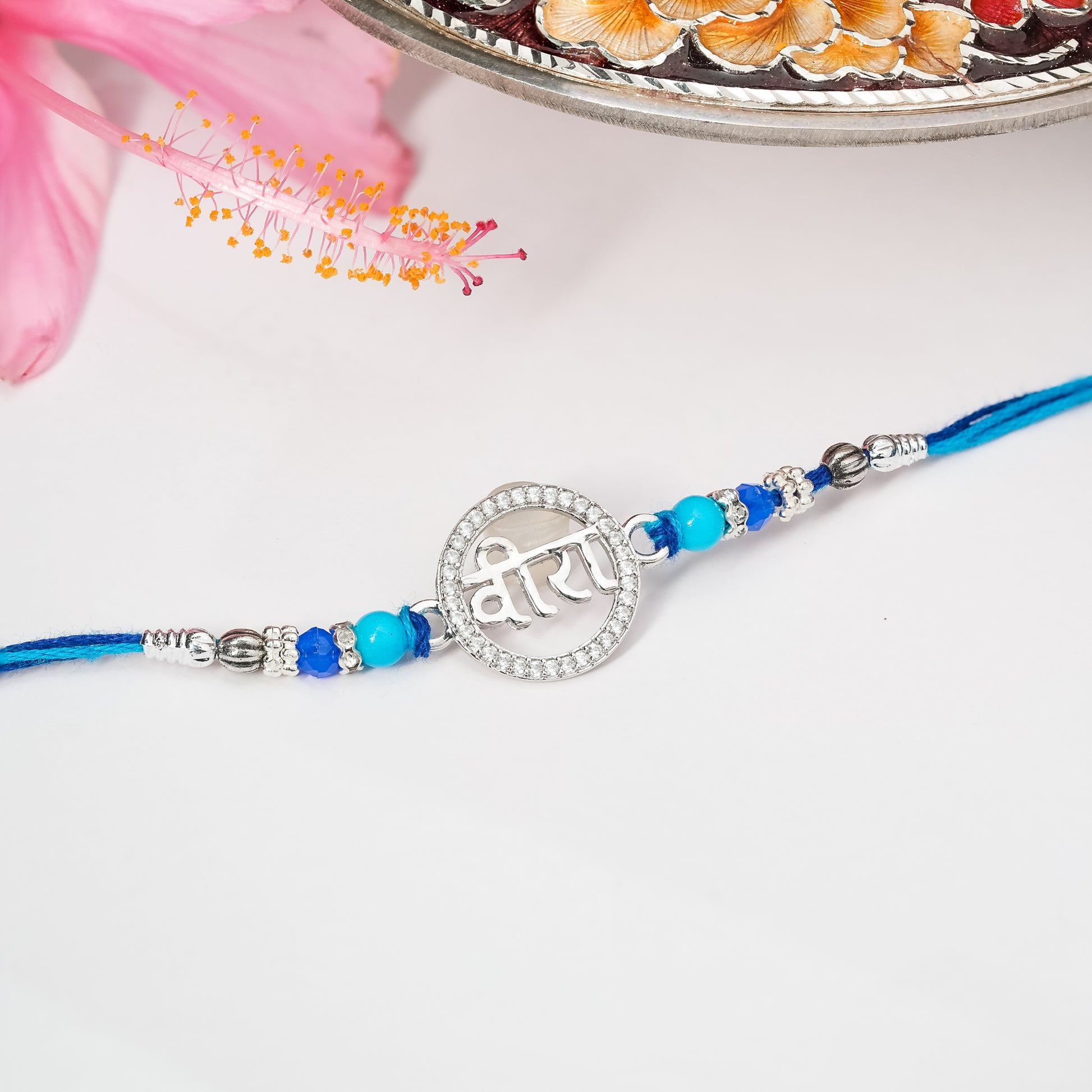 Rakhi in sterling silver with symbolic centerpiece tied on soft thread, displayed on plain background.

