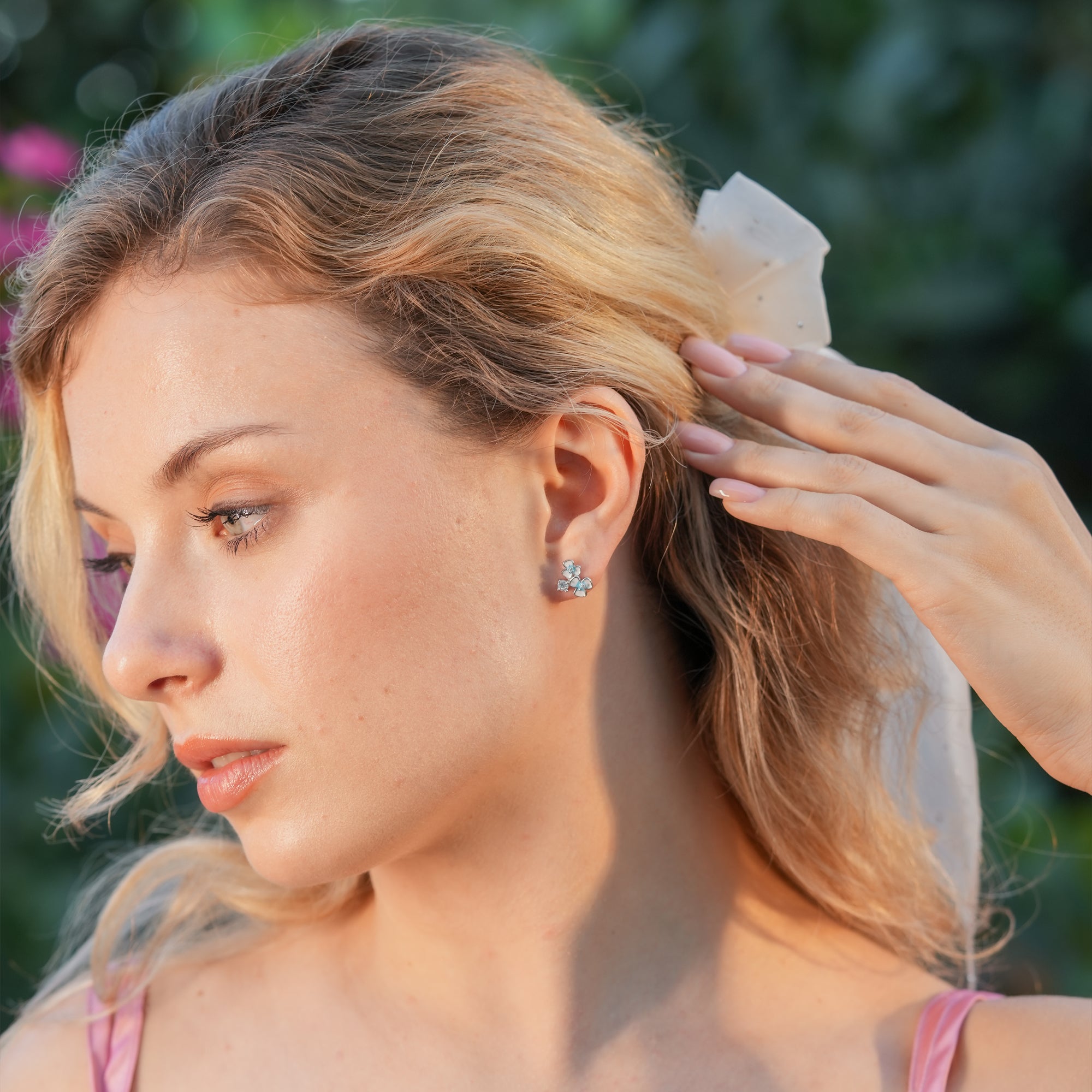 Floral enamel stud earrings styled on a woman with a soft updo and pastel outfit.