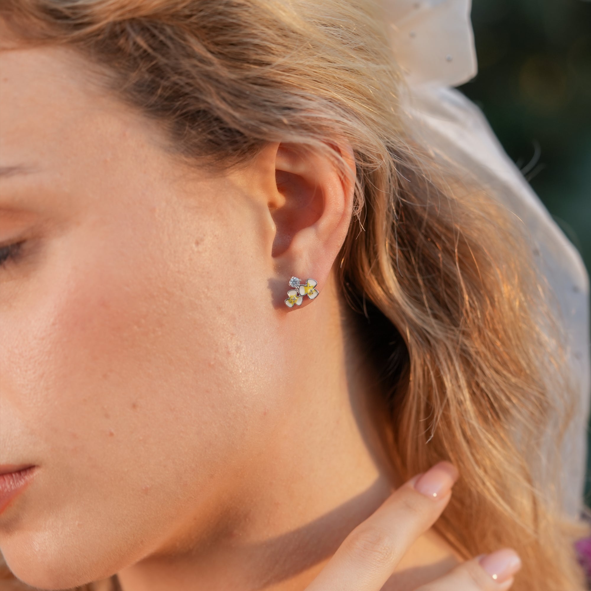Floral enamel stud earrings styled on a woman with a soft updo and pastel outfit.