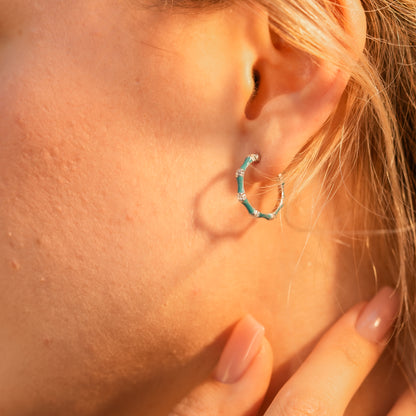 Turquoise enamel half-hoop earrings styled on a woman with a crisp summer outfit.